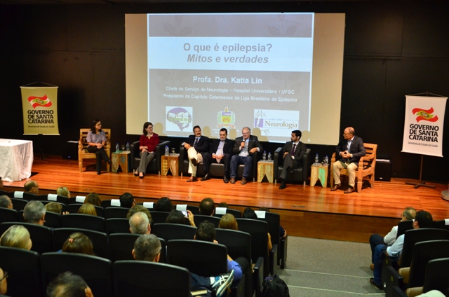 Autoridades e especialistas participam de simpósio sobre epilepsia no auditório do Centro Integrado de Cultura, em Florianópolis. Painel ao fundo exibe o tema 'O que é epilepsia? Mitos e verdades'.