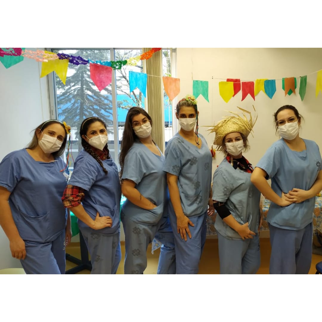 6 mulheres da saúde posam em foto. A sala está decorada com bandeiras coloridas típicas de festas juninas.