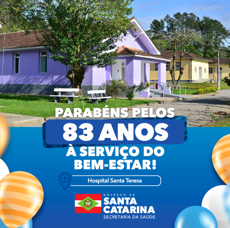 Imagem comemorativa dos 83 anos do Hospital Santa Teresa. Em primeiro plano, há uma faixa azul com balões coloridos nas laterais e o texto: "Parabéns pelos 83 anos a serviço do bem-estar! Hospital Santa Teresa". Abaixo, aparece a logomarca do Governo de Santa Catarina - Secretaria da Saúde. Ao fundo, uma foto do hospital com prédios em tons de roxo e amarelo, árvores e bancos brancos em um jardim bem cuidado.