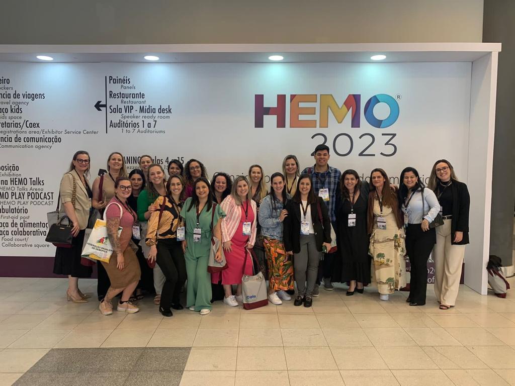 Grupo de profissionais posando para foto em frente ao painel do evento HEMO 2023.