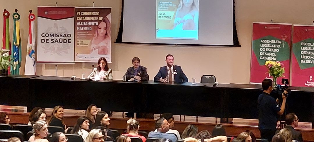 Mesa de abertura do VI Congresso Catarinense de Aleitamento Materno, com três palestrantes sentados e público assistindo no auditório da Assembleia Legislativa de Santa Catarina.