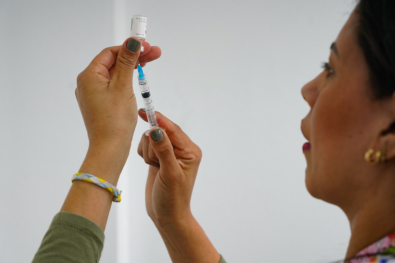 Profissional de saúde segurando frasco e seringa, preparando dose de vacina.