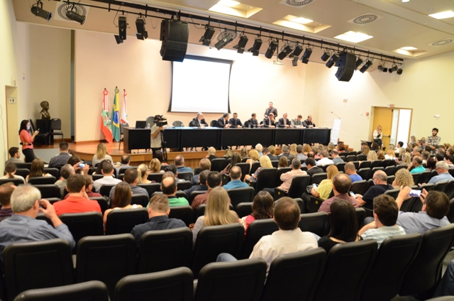 Audiência pública na Assembleia Legislativa de Santa Catarina, com auditório lotado e mesa composta por representantes do Poder Executivo, Ministério Público e deputados estaduais. A pauta discutida envolve repasses e dívidas do Estado com os municípios na área da saúde.