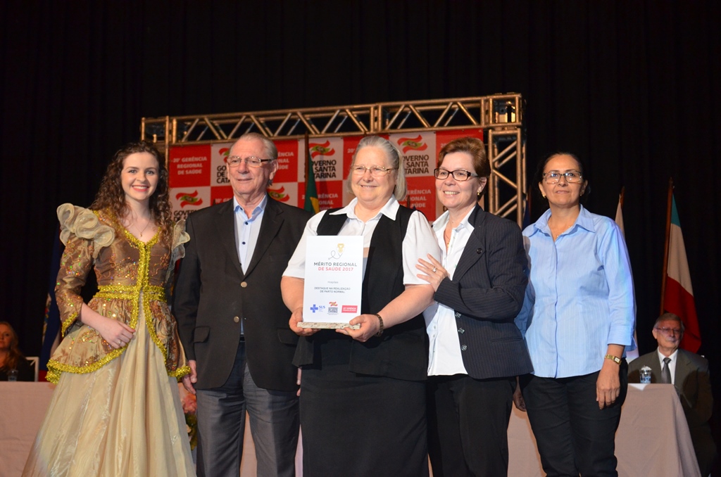 Cinco pessoas estão em pé no palco durante cerimônia de premiação.