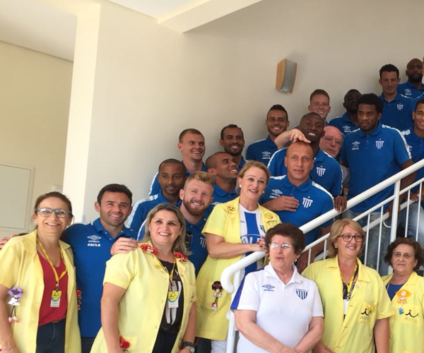 Jogadores do Avaí Futebol Clube posam sorridentes em uma escadaria com voluntárias e profissionais do Hospital Infantil Joana de Gusmão, durante visita em ação social comemorativa aos 91 anos do clube.