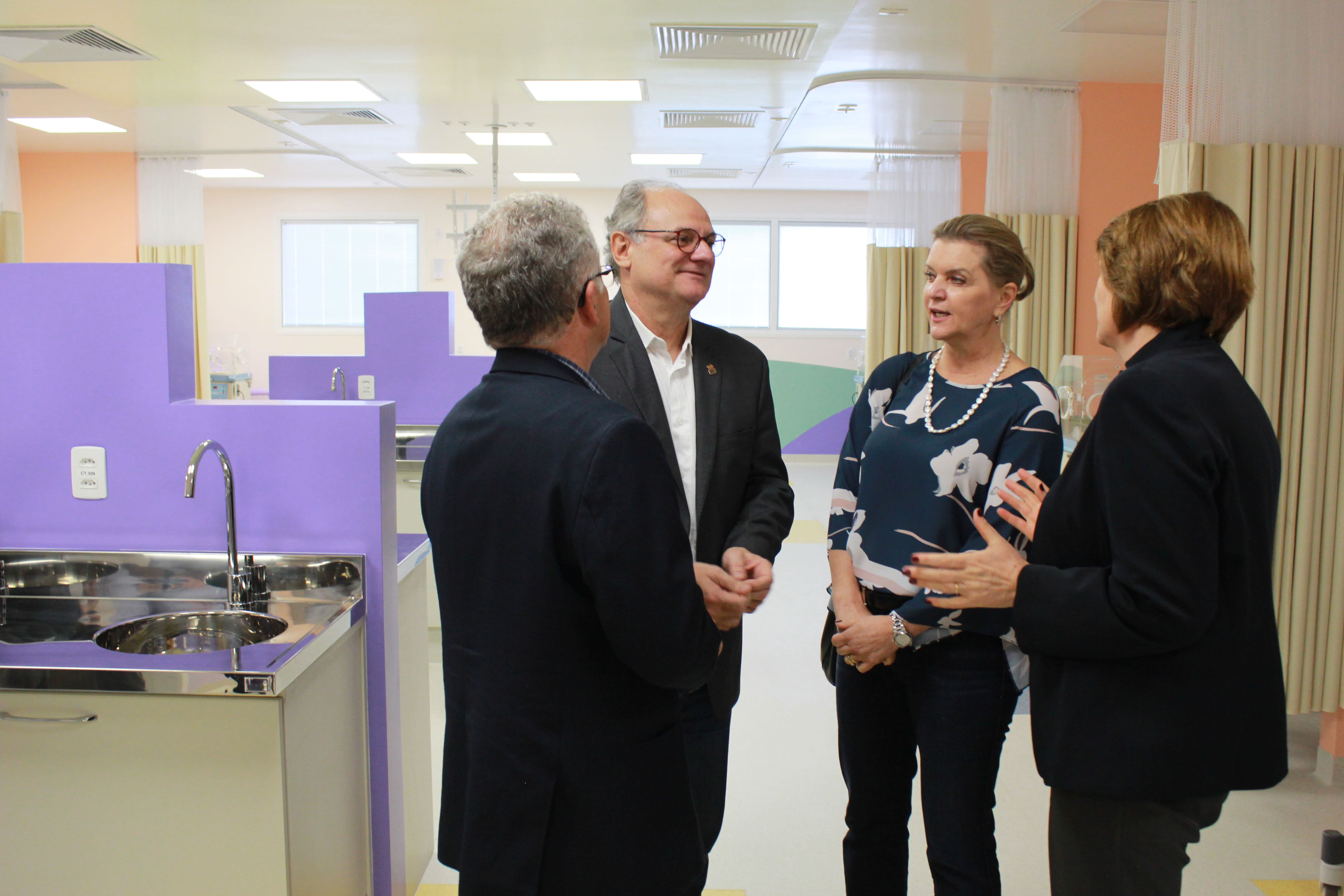 Secretário de Estado da Saúde e equipe visitam a nova UTI Neonatal do Hospital Infantil Dr. Jeser Amarante Faria, observando as instalações modernizadas com divisórias roxas e bancadas de inox.
