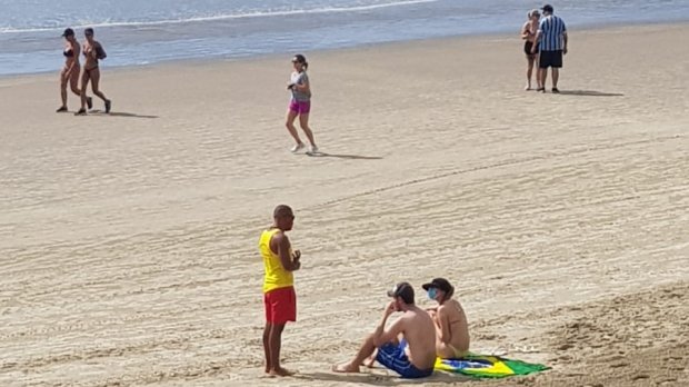 Salva-vidas fardados em conversa com grupo de banhistas na areia da praia, durante ação educativa sobre segurança e medidas preventivas em Santa Catarina.