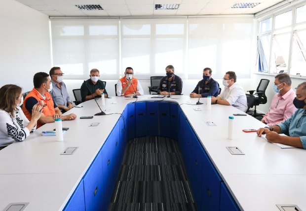 Autoridades da saúde de Santa Catarina reunidas em mesa de reunião, discutindo documentos em um ambiente profissional.