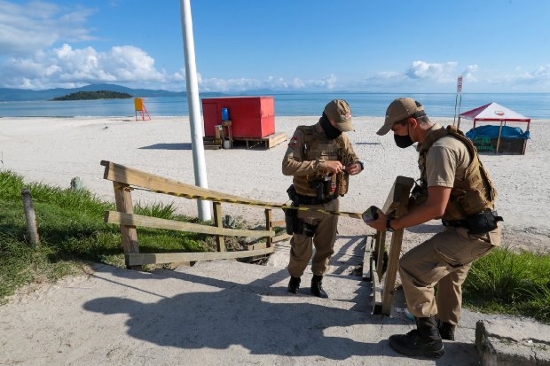 Agentes de segurança instalando faixa de restrição na entrada de praia em Santa Catarina, como parte das fiscalizações das medidas sanitárias durante a pandemia.