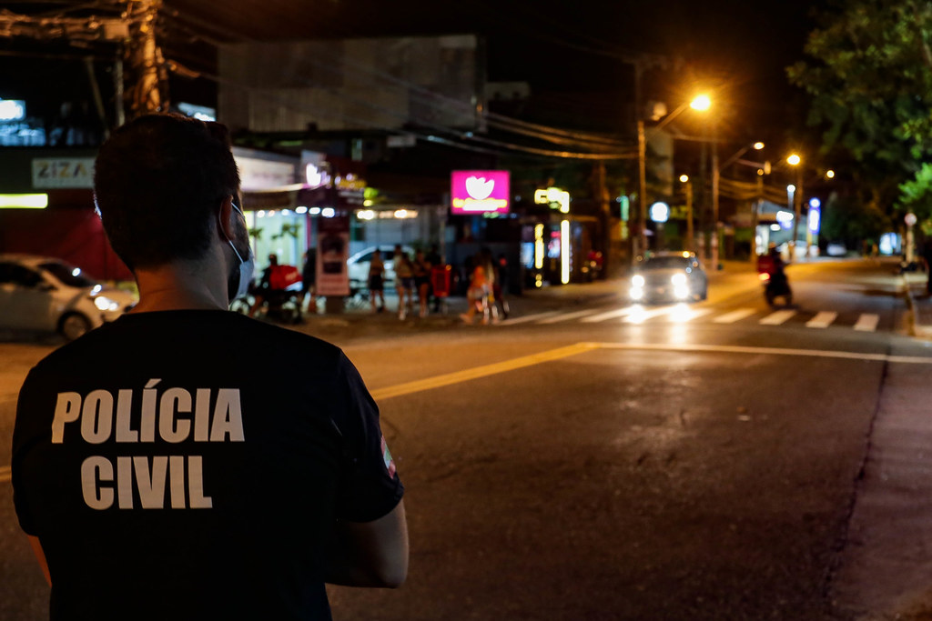 Agente de segurança em patrulha noturna observando movimento em rua urbana de Santa Catarina, durante fiscalização das medidas restritivas contra COVID-19.