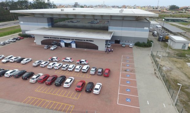 Vista aérea do Centro de Eventos Luiz Henrique da Silveira, mostrando a arquitetura moderna do prédio e o extenso estacionamento repleto de carros.