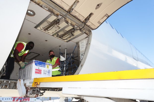 Homens desembarcam de um avião carregando uma caixa com doses da vacina Coronavac.