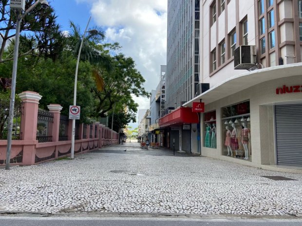 Foto de esquina de rua vazia, com um muro de casarão histórico em um lado e fachadas variadas de lojas no lado oposto.