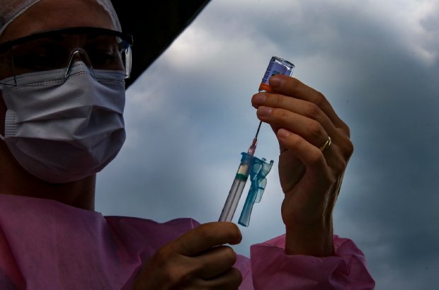 Profissional de saúde de máscara segurando seringa com vacina Coronavac.