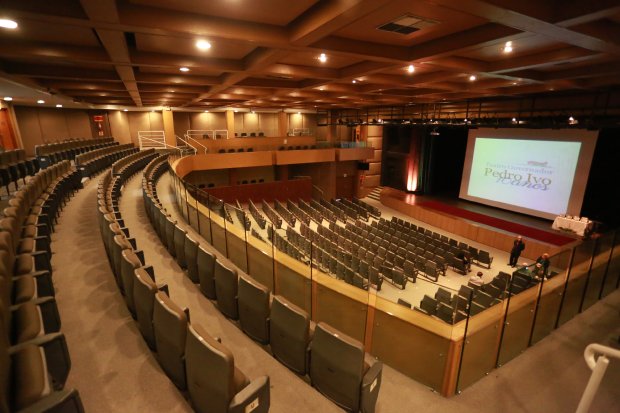Auditório vazio, com cadeiras desocupadas e palco sem pessoas, refletindo as restrições de eventos durante a pandemia de COVID-19 em Santa Catarina.