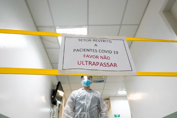 Médico de jaleco branco posicionado atrás de faixa com placa 'Favor não ultrapassar' em ambiente hospitalar.