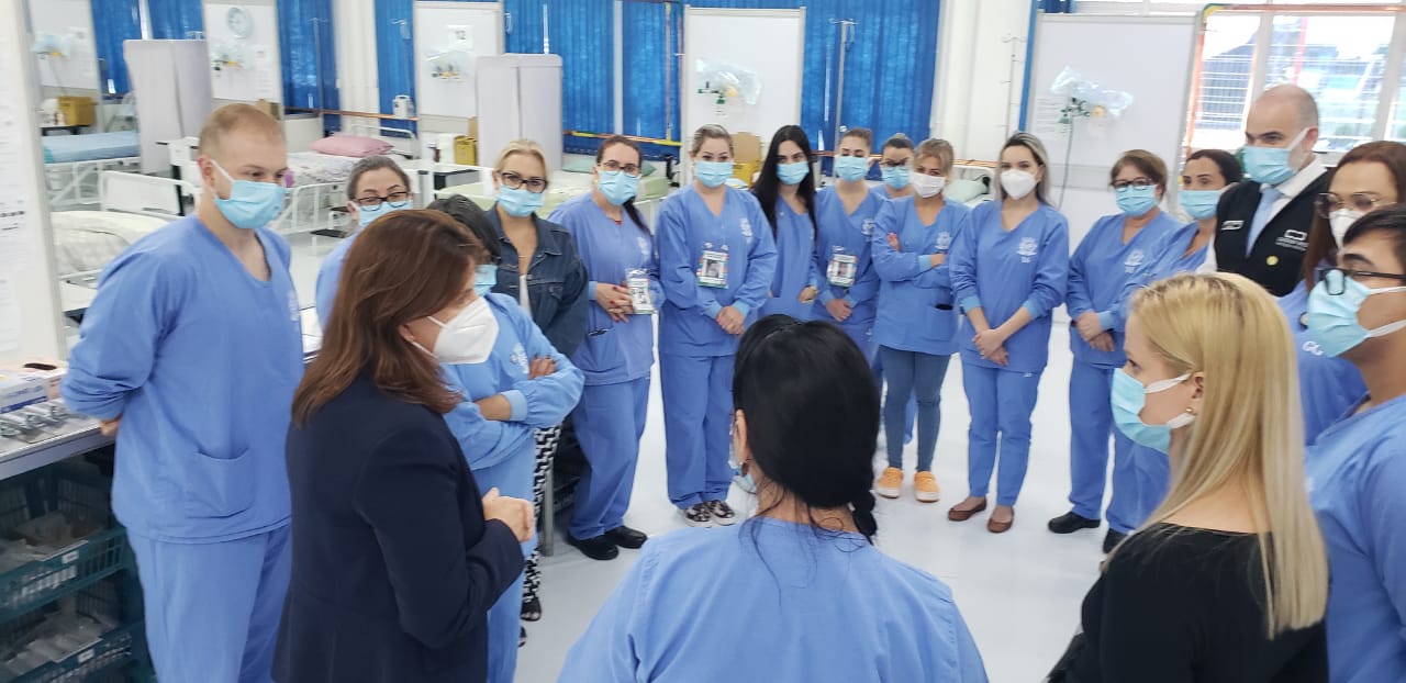 Secretária Carmen Zanotto de traje formal preto posa com equipe de saúde em centro de atendimento COVID-19 na região Oeste, durante visita de inspeção às instalações.