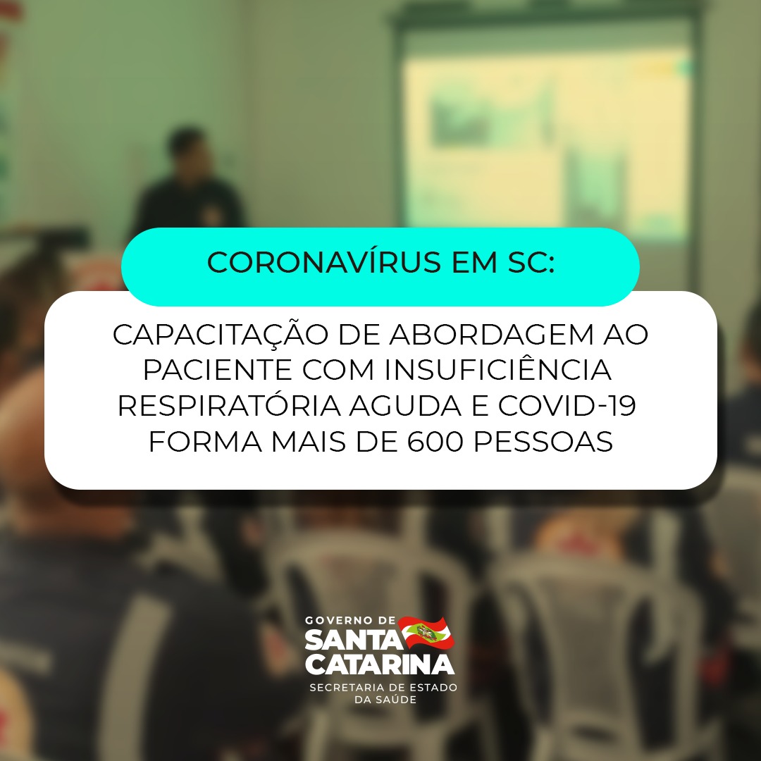 Sala de capacitação com profissionais de saúde sentados em cadeiras de plástico brancas, assistindo a uma apresentação sobre o manejo de pacientes com COVID-19 e insuficiência respiratória aguda. À frente, um palestrante utiliza um projetor para exibir slides educativos. No rodapé da imagem, o texto diz: 'Coronavirus em SC: Capacitação de abordagem ao paciente com insuficiência respiratória aguda e Covid-19 forma mais de 600 pessoas'.