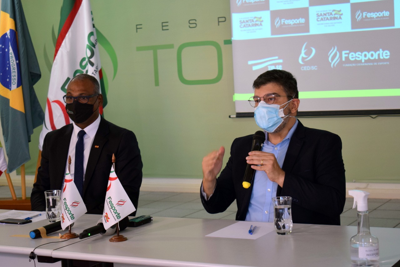 Kelvin Soares e Eduardo Macário durante coletiva de imprensa, anunciando a retomada das atividades esportivas em Santa Catarina. Ao fundo, um projetor exibe os logos do Governo do Estado e da Fesporte (Fundação Catarinense de Esporte).