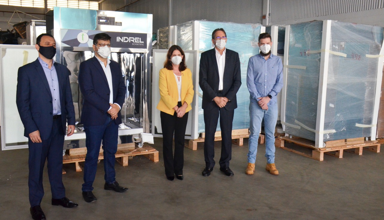 Cinco pessoas posam em frente a câmaras frias para armazenamento de vacinas, em evento de doação ao Governo de Santa Catarina. Destaque para a secretária da Saúde, vestindo um blazer amarelo, ao centro do grupo.