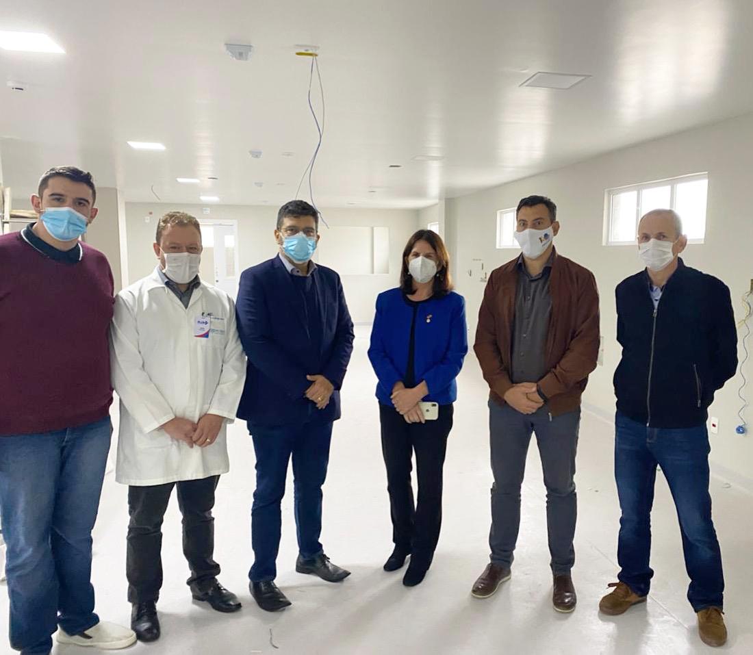A secretária da Saúde de Santa Catarina posa em uma sala branca com cinco homens, durante visita a hospitais da região Oeste e Serra Catarinense em 2021.