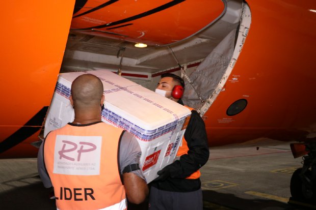 Dois homens retirando caixa térmica de avião laranja. Eles estão de coletes laranja.