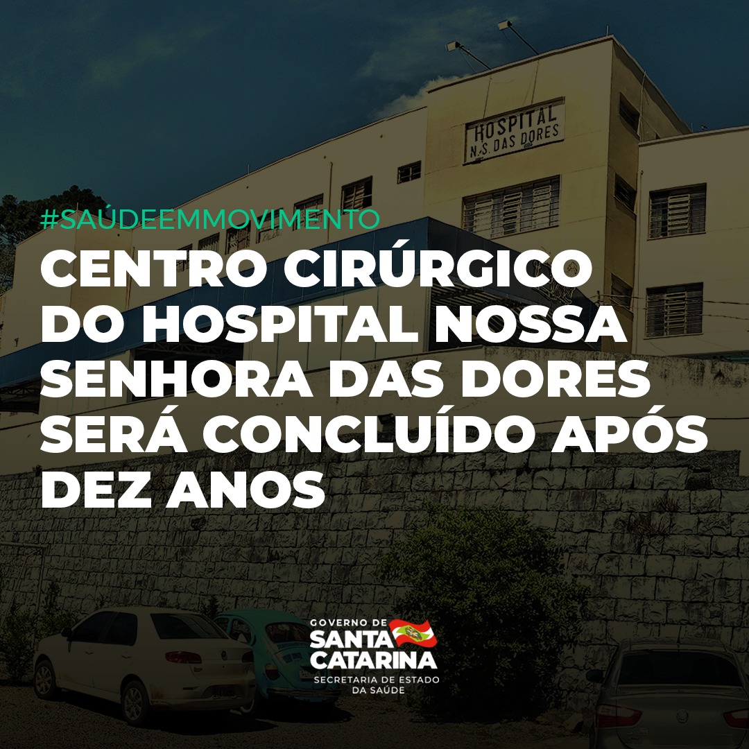 Fachada do Hospital Nossa Senhora das Dores com destaque para o anúncio de que o centro cirúrgico será concluído após dez anos. Em primeiro plano, carros estacionados e uma árvore; ao fundo, o céu azul com algumas nuvens.
