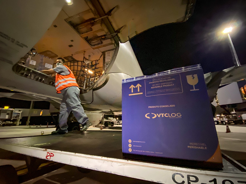 Pessoa com colete laranja retirando caixas de produtos congelados do avião.