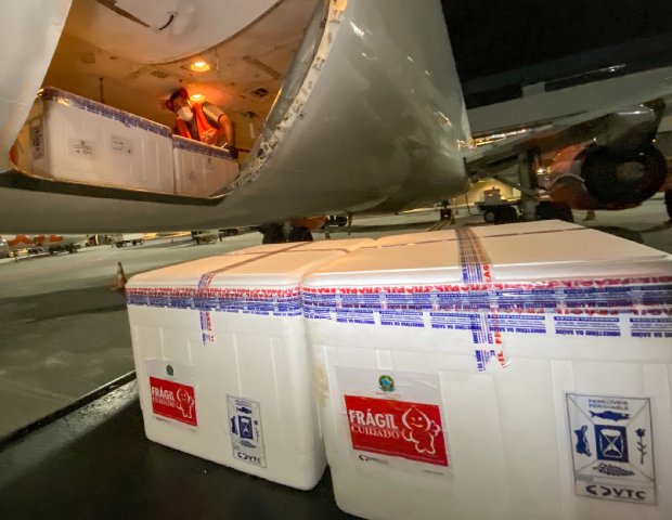 Avião com portas abertas, existem caixas dentro e fora dele e uma pessoa dentro segurando uma caixa.