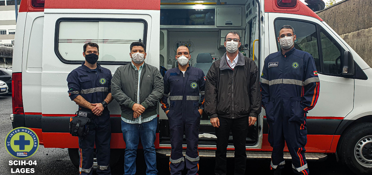 5 homens de máscara posando em frente a uma ambulância
