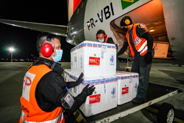 Três homens com coletes laranja retirando caixas térmicas brancas de avião 