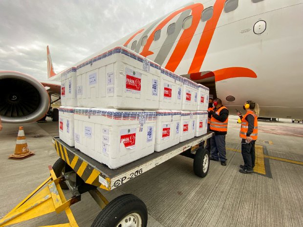 Caixas térmicas sendo retiradas do avião por homem e mulher de colete laranja 