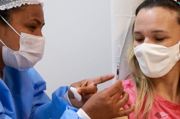 Profissional de azul mostrando para pessoa que vai receber a vacina a seringa que será aplicada.