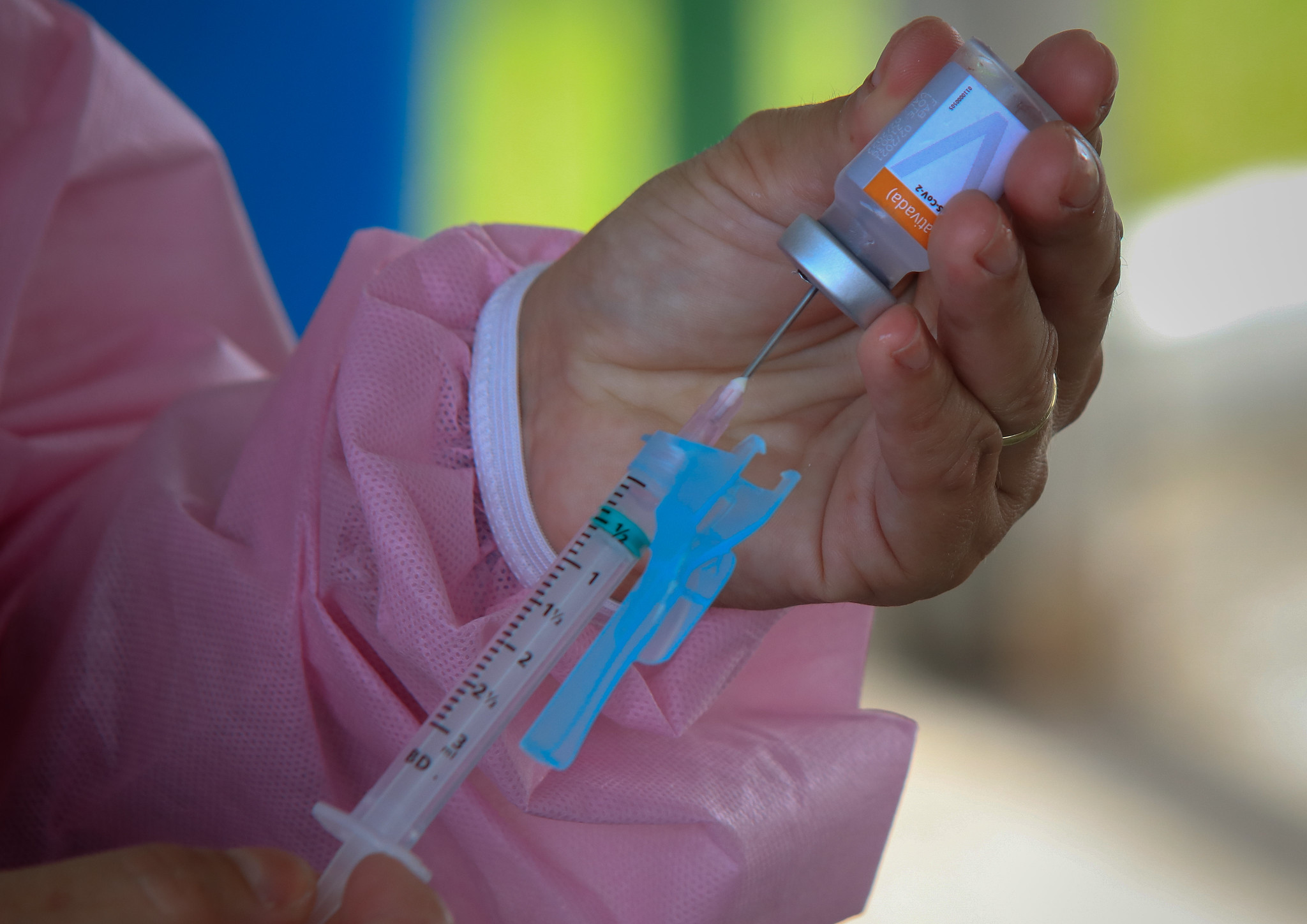 Mão segurando uma seringa sendo preenchida com dose de vacina retirada de um frasco.