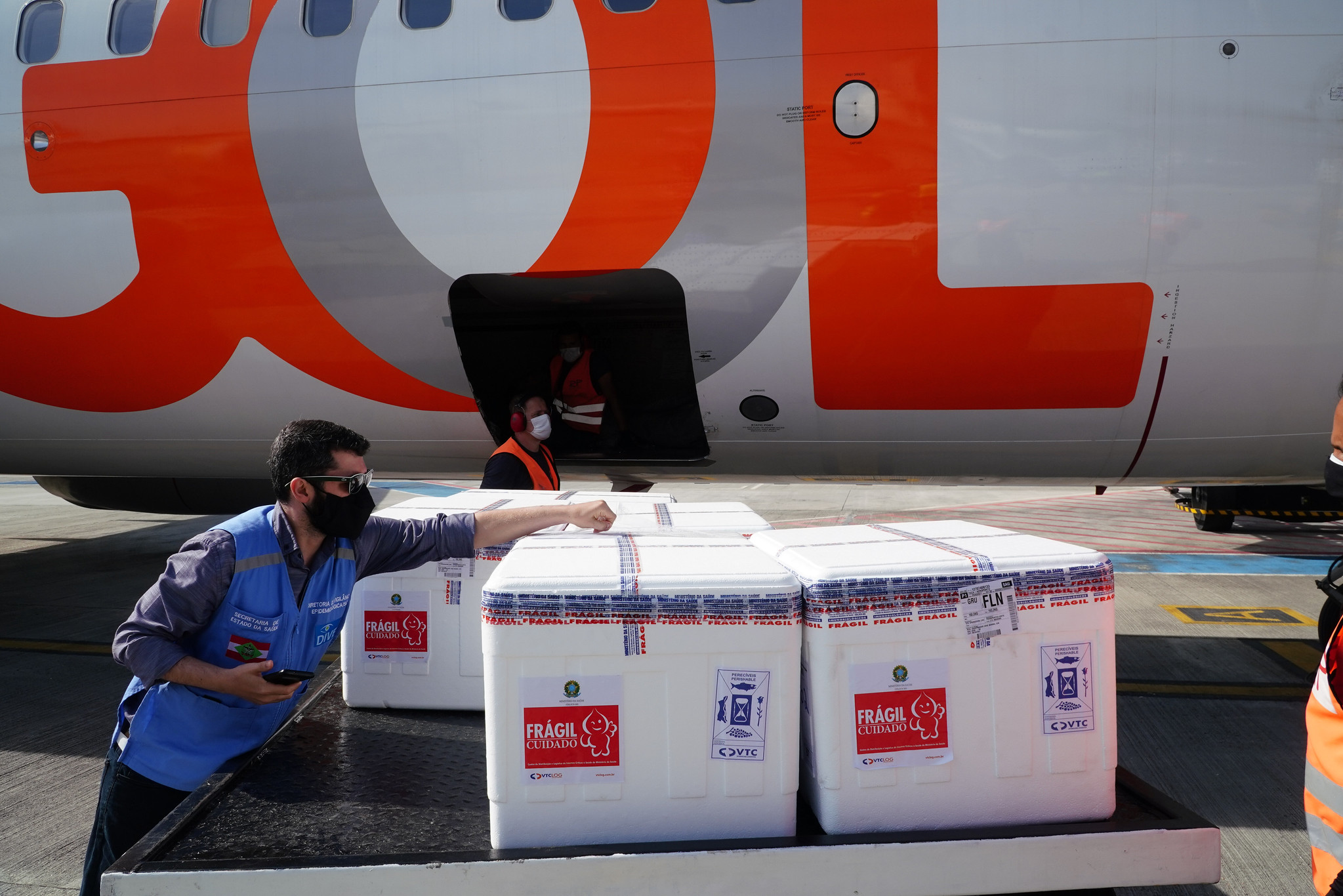 Homem com colete azul descarregando caixas brancas do avião branco da Gol