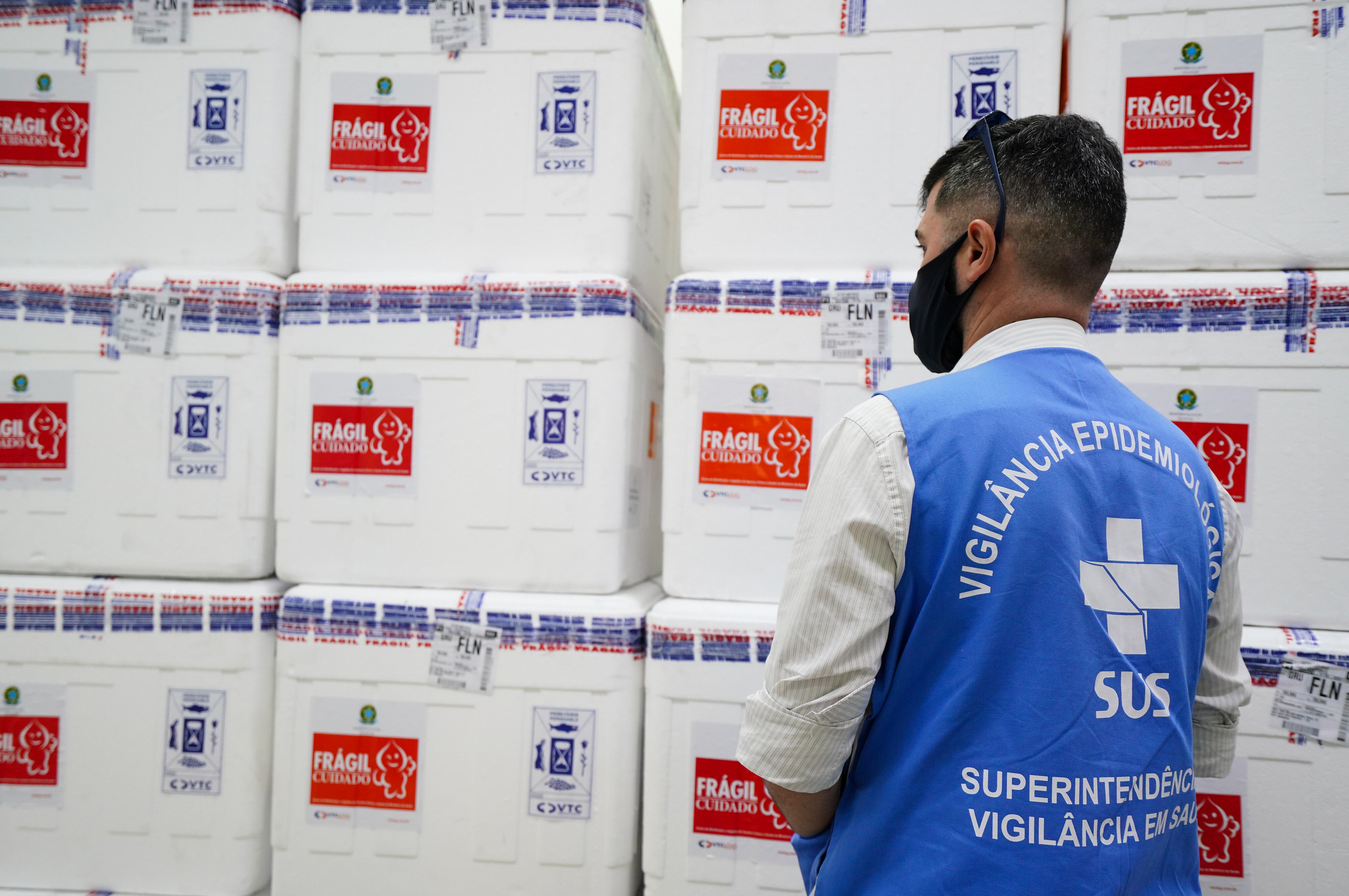 Homem com colete azul da vigilância epidemiológica observando caixas térmicas brancas