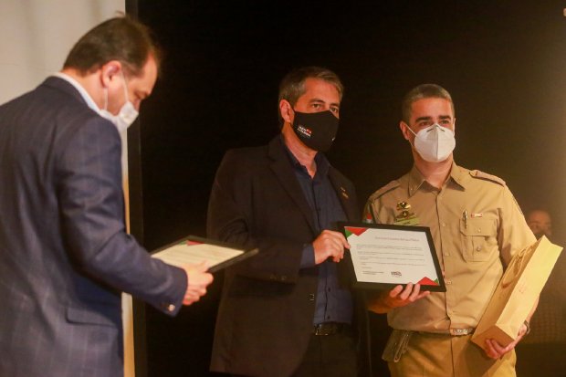 3 autoridades segurando documentos emoldurados