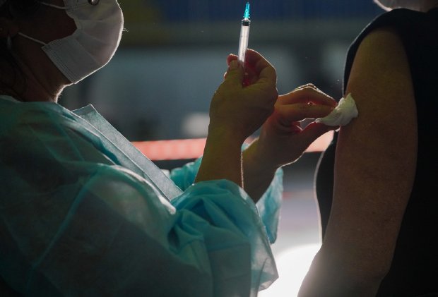 Profissional da saúde limpando ombro de homem com algodão no lugar onde aplicou uma vacina.