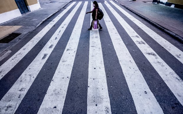 Mulher com sacola roxa atravessando rua na faixa de pedestre 