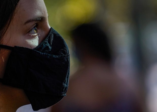 Perfil de mulher olhando para a esquerda com luz solar iluminando seu rosto, tendo praia e folhas de coqueiro ao fundo, simbolizando a continuidade das medidas de combate à COVID-19 em Santa Catarina durante o verão.