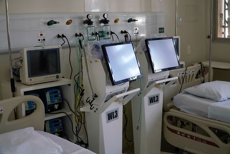 Leitos hospitalares equipados com monitores, ventiladores mecânicos e outros aparelhos médicos ao lado das camas. O ambiente é limpo e bem iluminado, com equipamentos organizados e prontos para uso em pacientes.