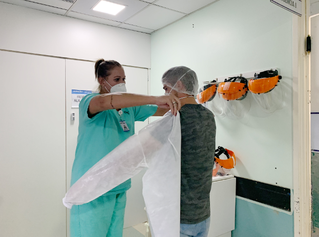Profissional de saúde vestindo traje verde de proteção completa ajudando outro colega a vestir.
