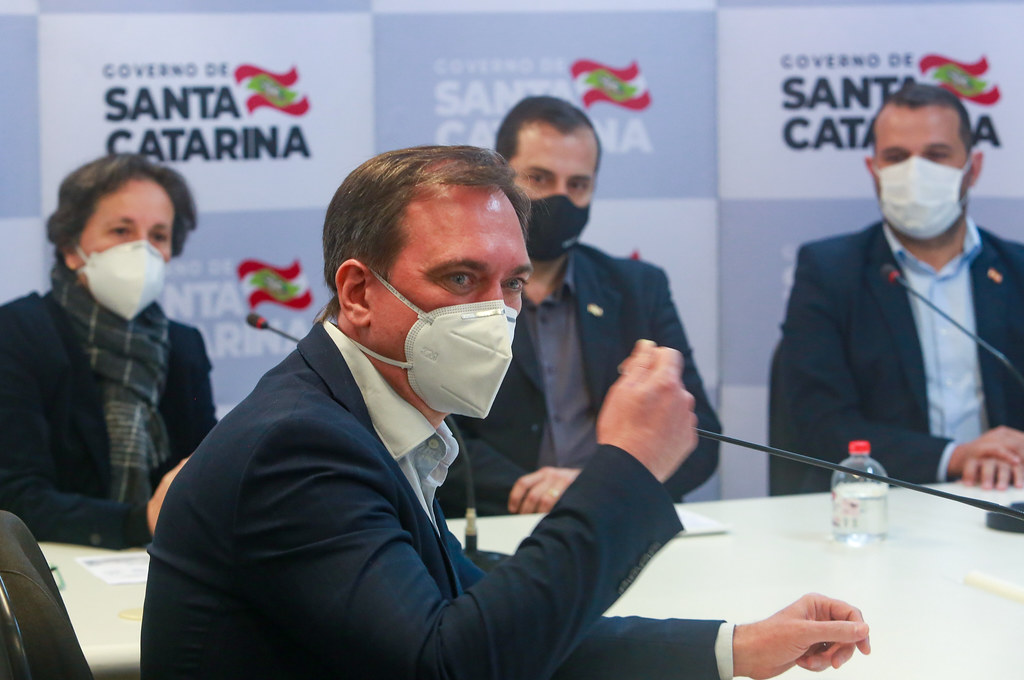 Pessoas em coletiva de imprensa, ao fundo, diversas logos do Governo de Santa Catarina