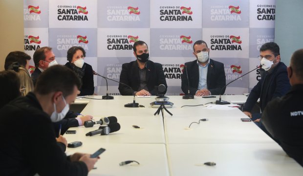 Pessoas em coletiva de imprensa, ao fundo, diversas logos do Governo de Santa Catarina