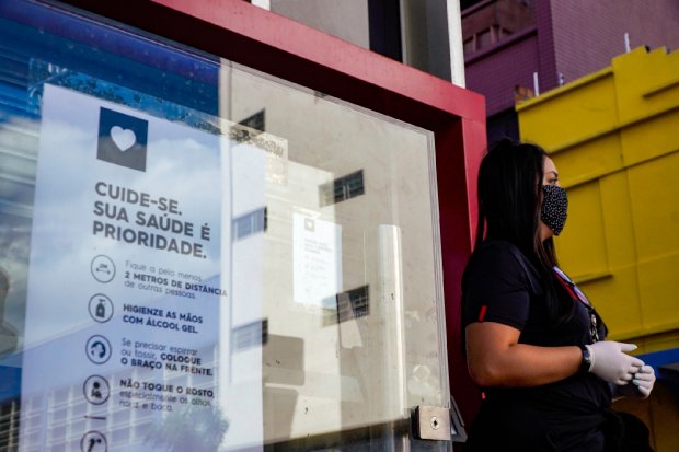 Mulher com roupas e máscara preta e luvas brancas, ao seu lado um painel de vidro.